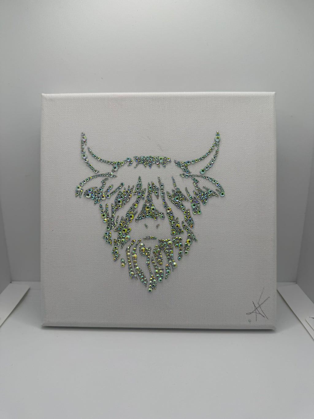 Decorative wall art with a highland coo design made of rhinestones on a white canvas background
