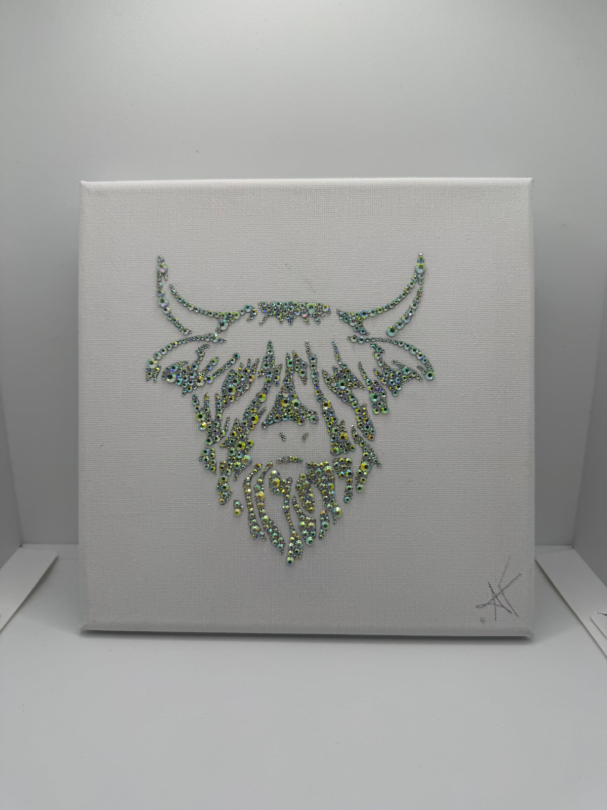 Decorative wall art with a highland coo design made of rhinestones on a white canvas background