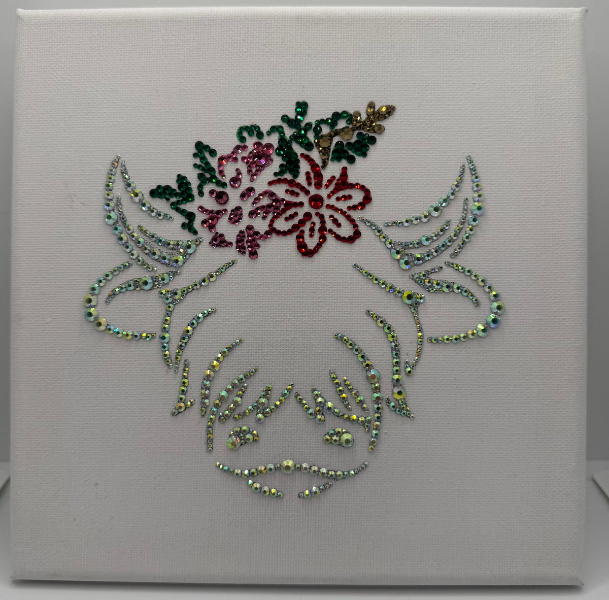 Decorative highland cow with floral design and rhinestones on a white canvas background